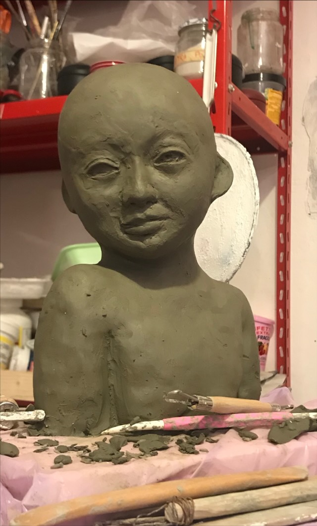 Unfired clay bust of a child, modelling tools on the table in front of it