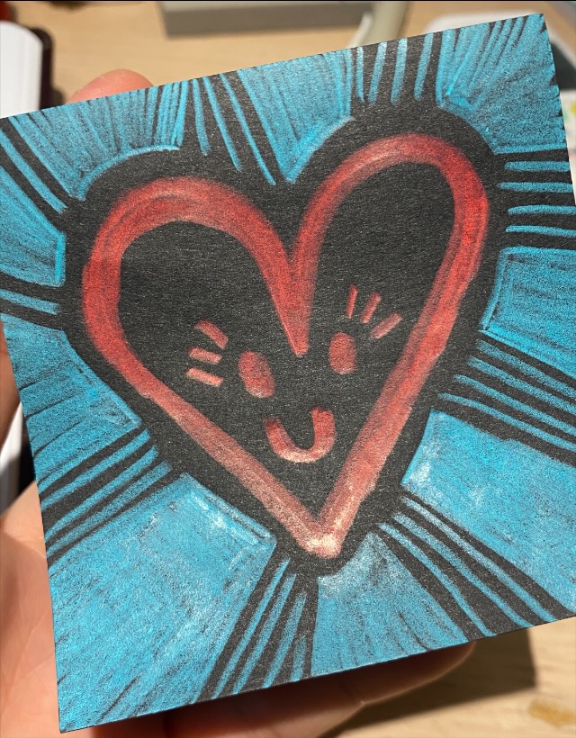 A small card with a red heart with a face on it, black ground, blue rays behind